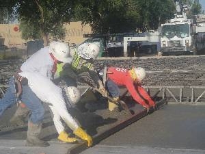 Construction workers in hard hats drag level over freshly poured concrete