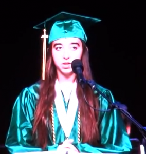 Teenage girl in green graduation cap and gown speaking at graduation ceremony