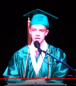 Teenage boy in green graduation cap and gown speaking at graduation ceremony