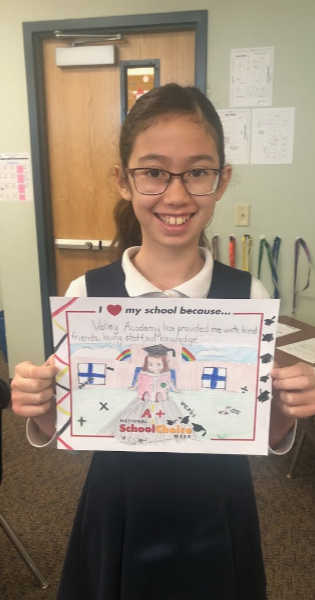 Smiling girl with glasses holds sign "Valley Academy has provided me with kind friends, loving staff, and knowledge!