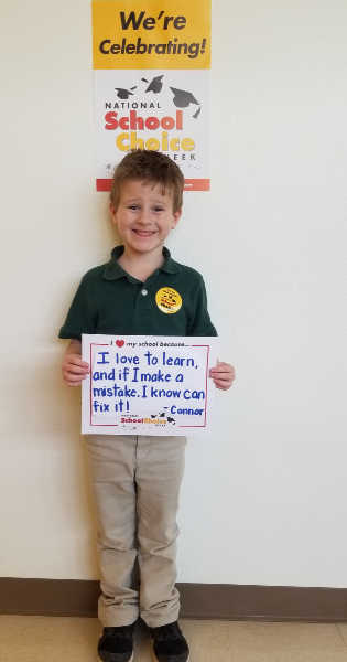 Smilling kindergarten boy holds sign "I love to learn, and if I make a mistake, I know I can fix it --Connor"