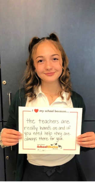 Middle school girl holds sign "I love my school becuase the teachers are really hands on and if you need help, they are always there for you."