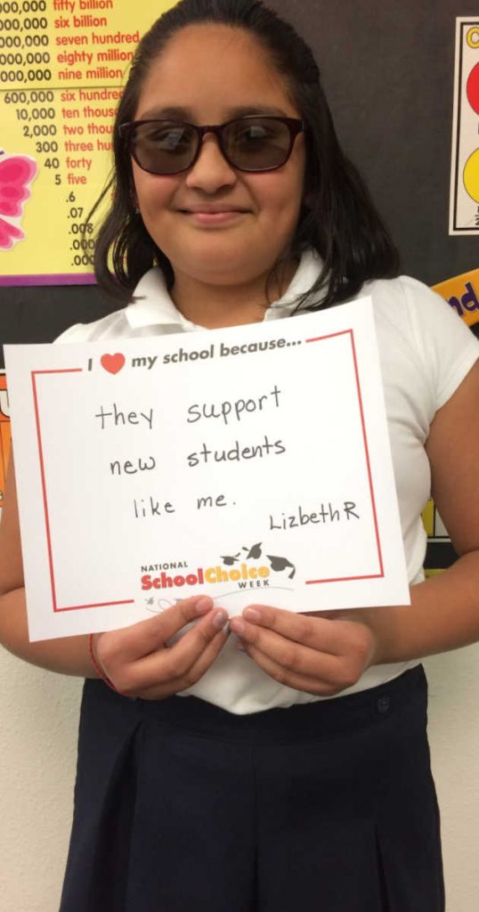 MIddle school girl with dark glasses holds sign "I love my school becuase they support new students like me. __Lizbeth R."