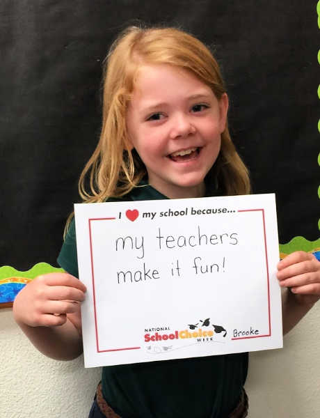 Smiling kindergarten girl holds sign "My teachers make it fun"